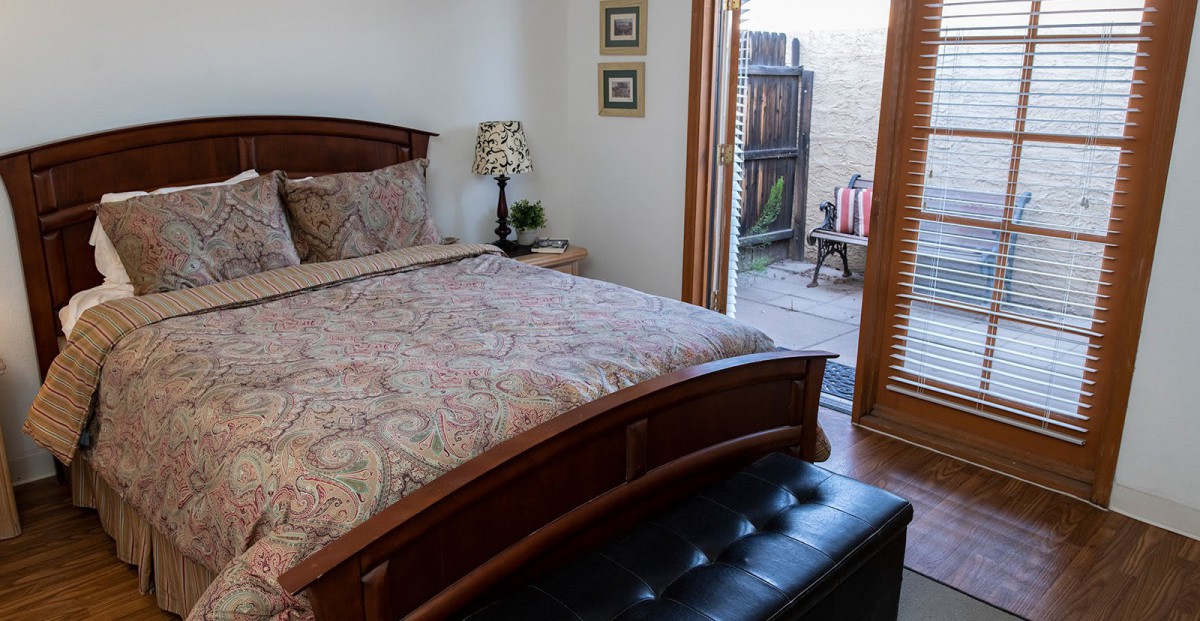 A cozy bedroom with a wooden bedframe, patterned bedding, and access to an outdoor patio.