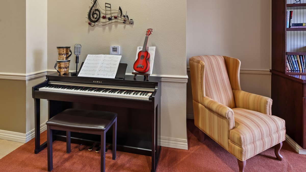 A cozy music room featuring a piano with sheet music and a red ukulele, complemented by a comfortable armchair.