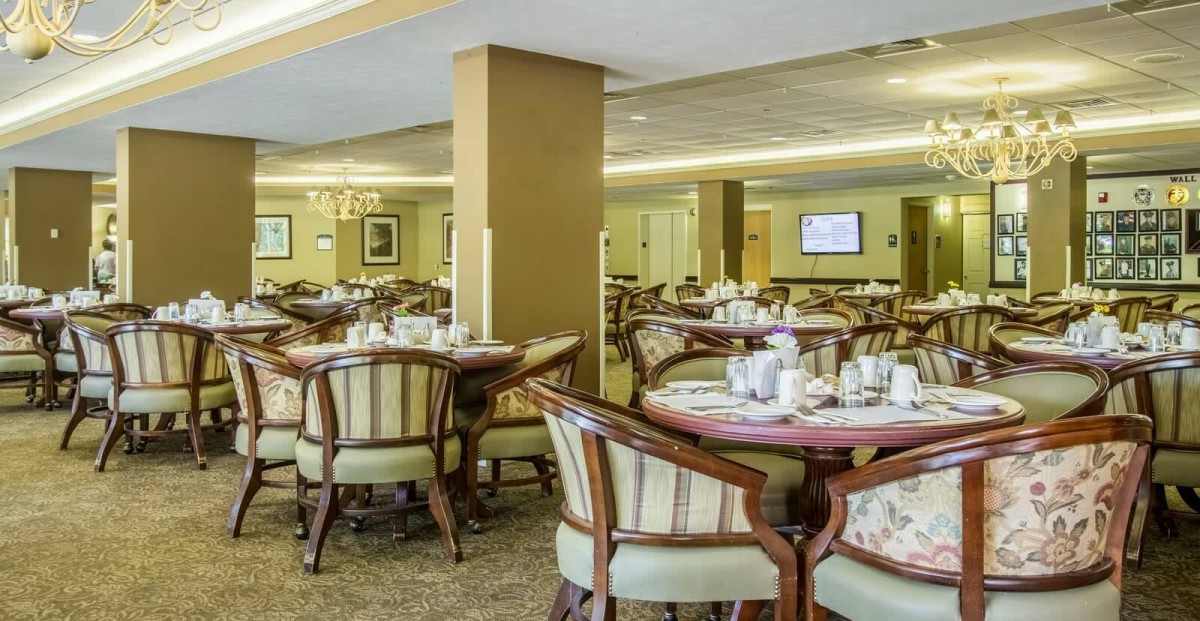 A spacious dining area with elegantly arranged tables and chairs, featuring soft lighting and a carpeted floor.