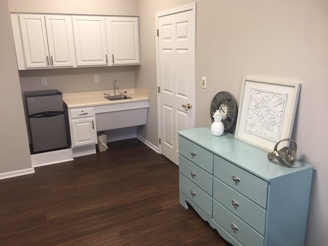 A kitchenette with a sink, white cabinets, refrigerator, and a blue dresser with decor in a home interior.