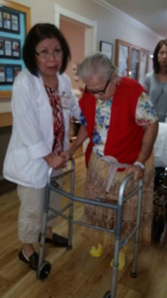 A healthcare worker assists an elderly person using a walker.