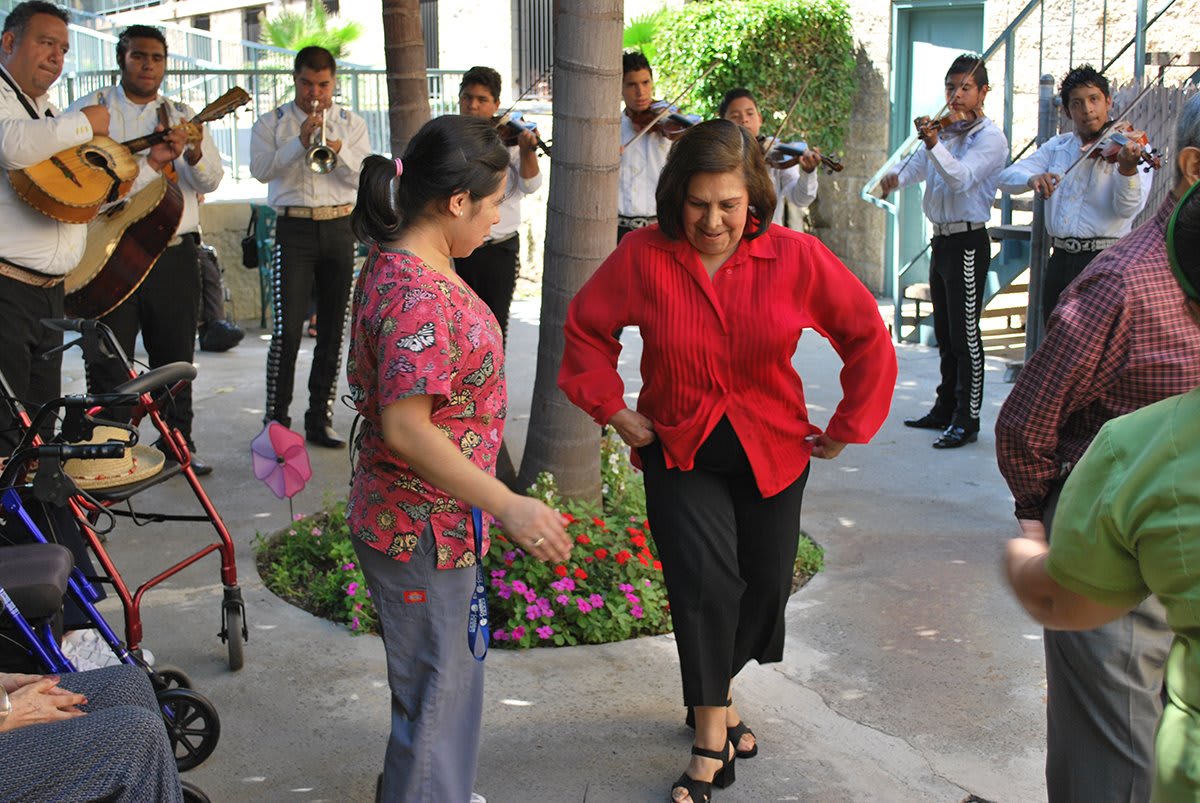Two women dance joyfully to live music in an outdoor celebration.