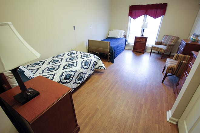 A simple bedroom with two beds, a chair, and a wooden floor.
