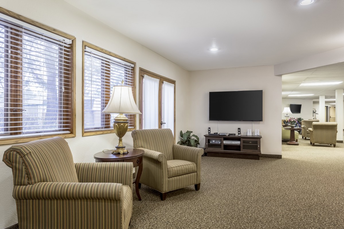 A cozy living room with armchairs, a lamp, and a wall-mounted television.