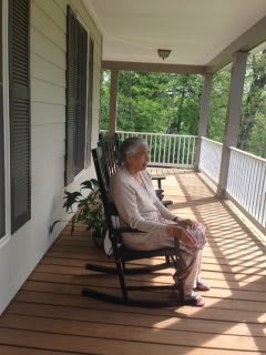 An elderly person sitting in a rocking chair on a porch, enjoying the outdoors.