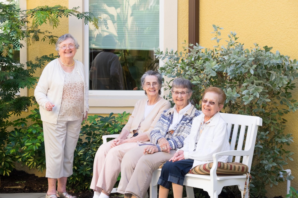 A group of senior women sitting on a bench outside, enjoying a sunny day.