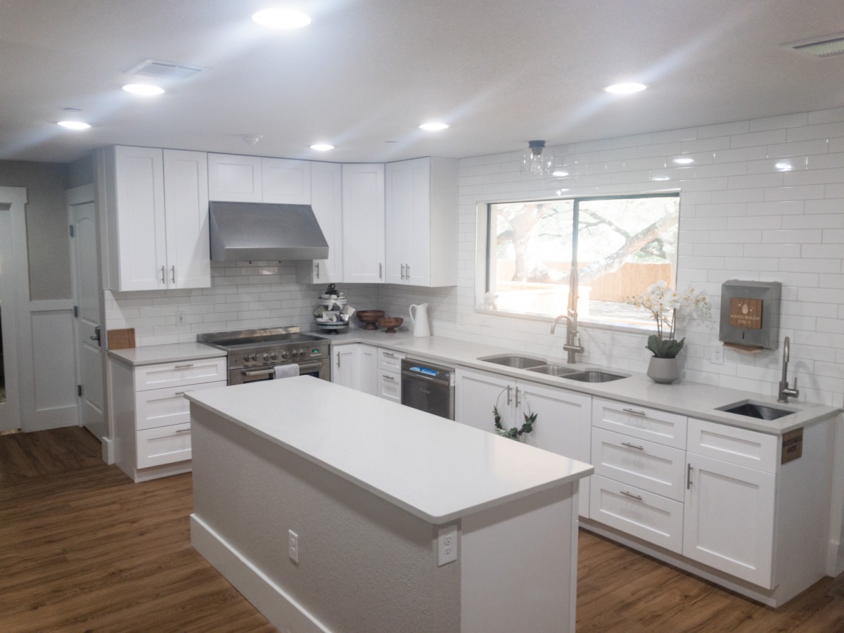 A modern kitchen with white cabinets and a central island, featuring stainless steel appliances and bright lighting.