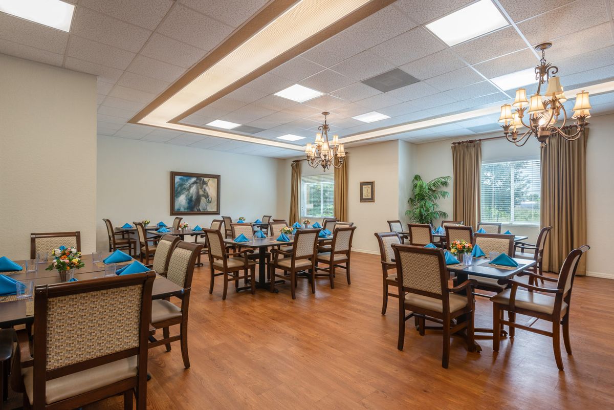 A well-lit dining room with neatly arranged tables and chairs, featuring wooden flooring and elegant lighting fixtures.