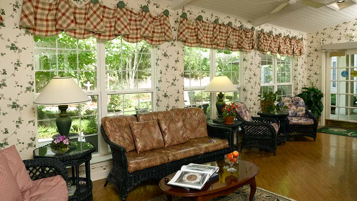 A cozy living room with floral wallpaper, featuring large windows, a patterned sofa, and a coffee table.