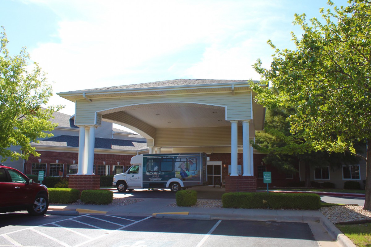 A building entrance with a van parked outside and trees in the background.