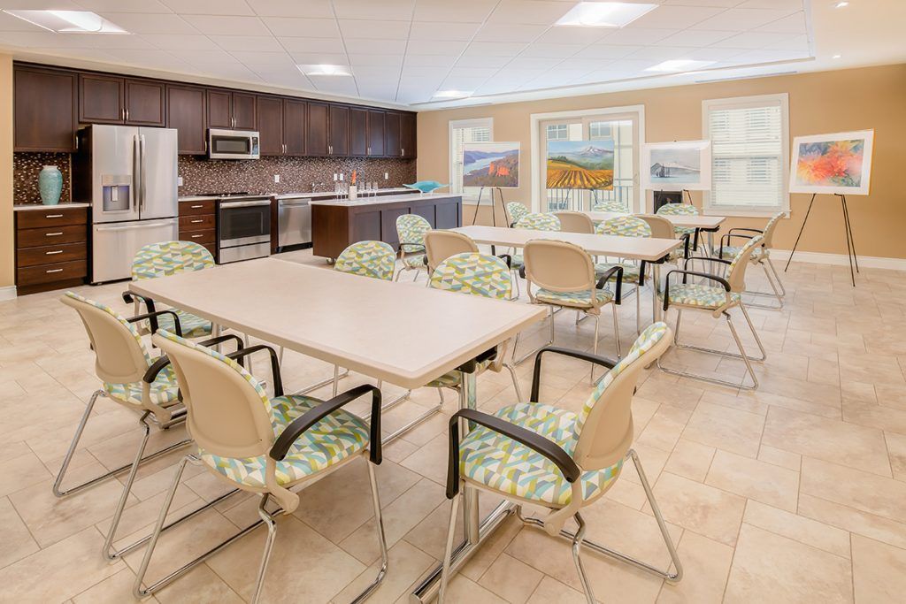 A modern dining room with multiple tables and chairs, adjacent to a kitchen area featuring colorful artwork.
