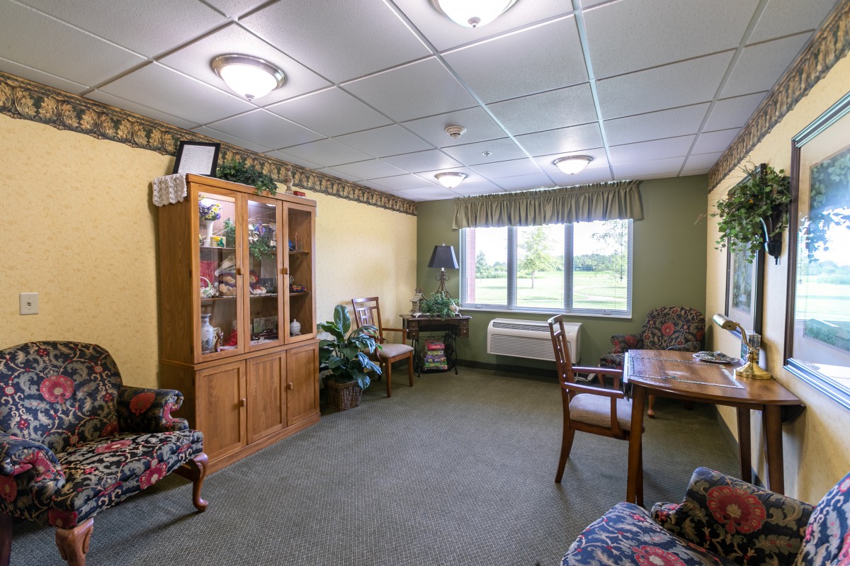 A cozy living room with a bookcase and seating area, featuring natural light from the window.
