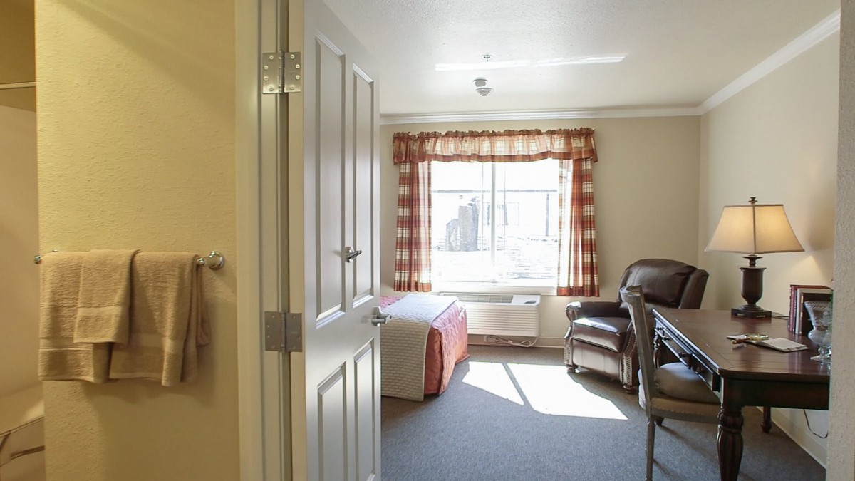 A bright bedroom with a bed and chair in natural light.