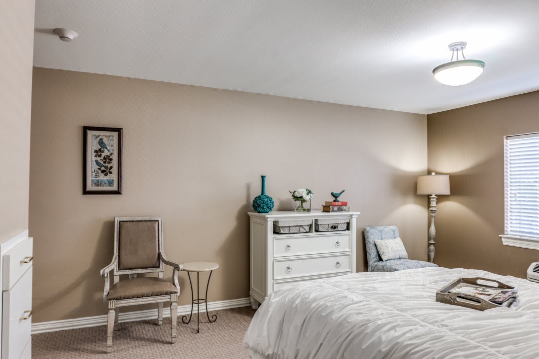 A cozy bedroom featuring a bed, dresser, and seating area with decorative elements.