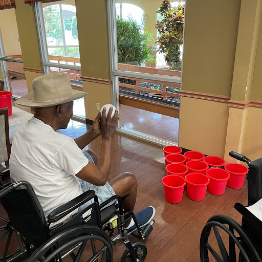 An engaging indoor activity where a person in a wheelchair is participating in a game involving tossing a ball into red buckets.