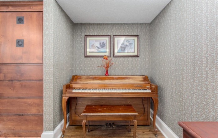 A wooden piano with a matching bench in a cozy indoor setting, adorned with decorative paintings and a flower vase.