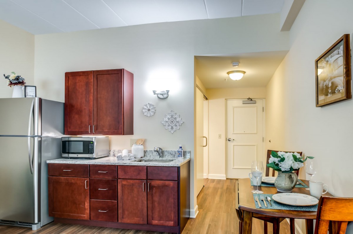 A cozy apartment kitchen featuring dark wood cabinets, a microwave, a sink, and a small dining table with chairs.