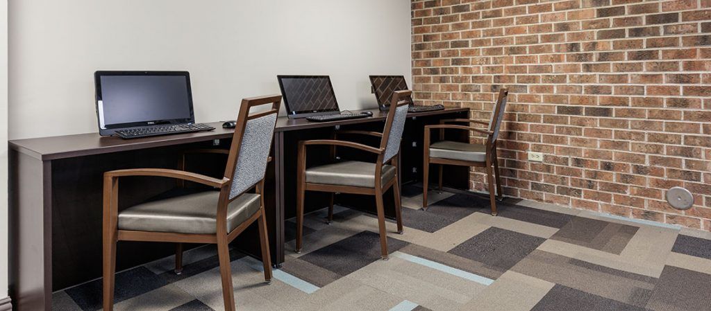 A modern workspace with multiple computers and chairs arranged neatly along a brick wall.