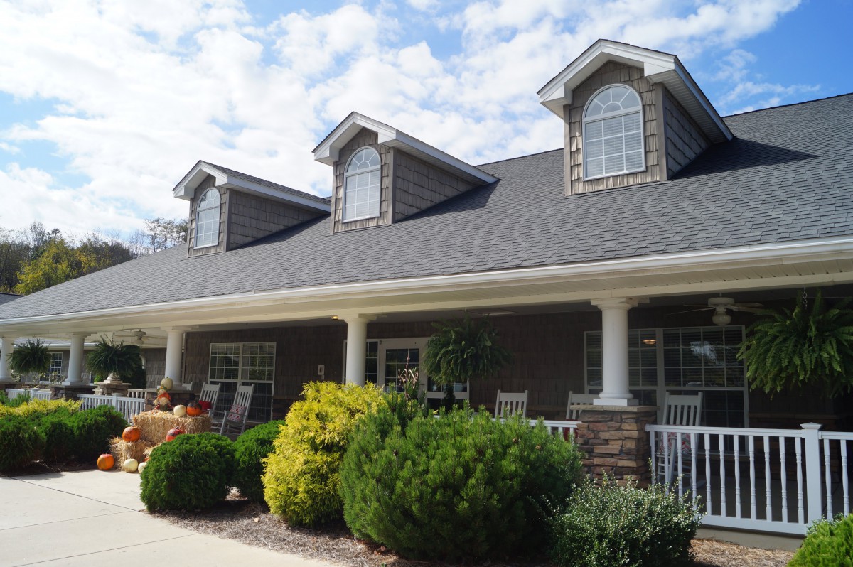 A suburban house with a sloped roof and front porch, surrounded by well-maintained landscaping.
