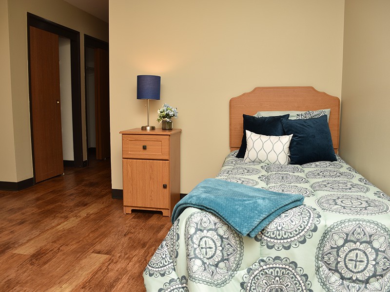 A cozy bedroom with a single bed, nightstand, and lamp.