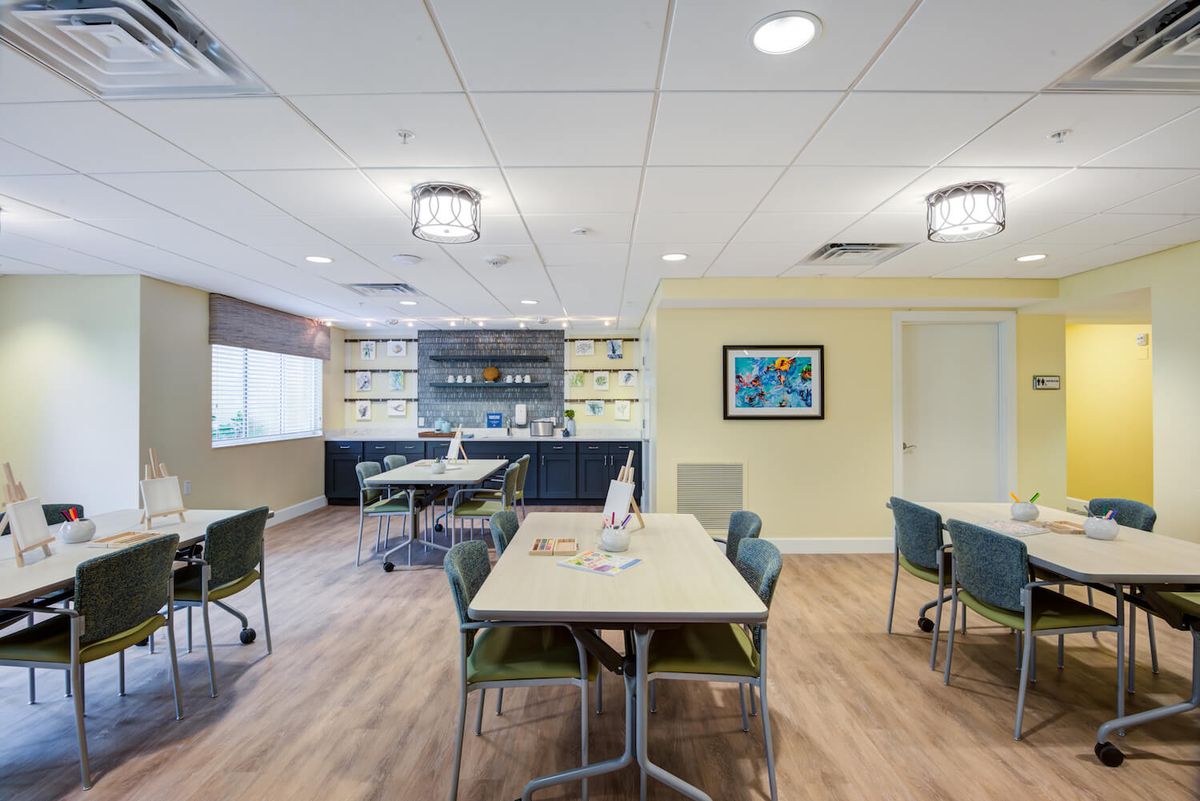 A modern meeting room with tables and chairs, featuring ample lighting and a wooden floor.