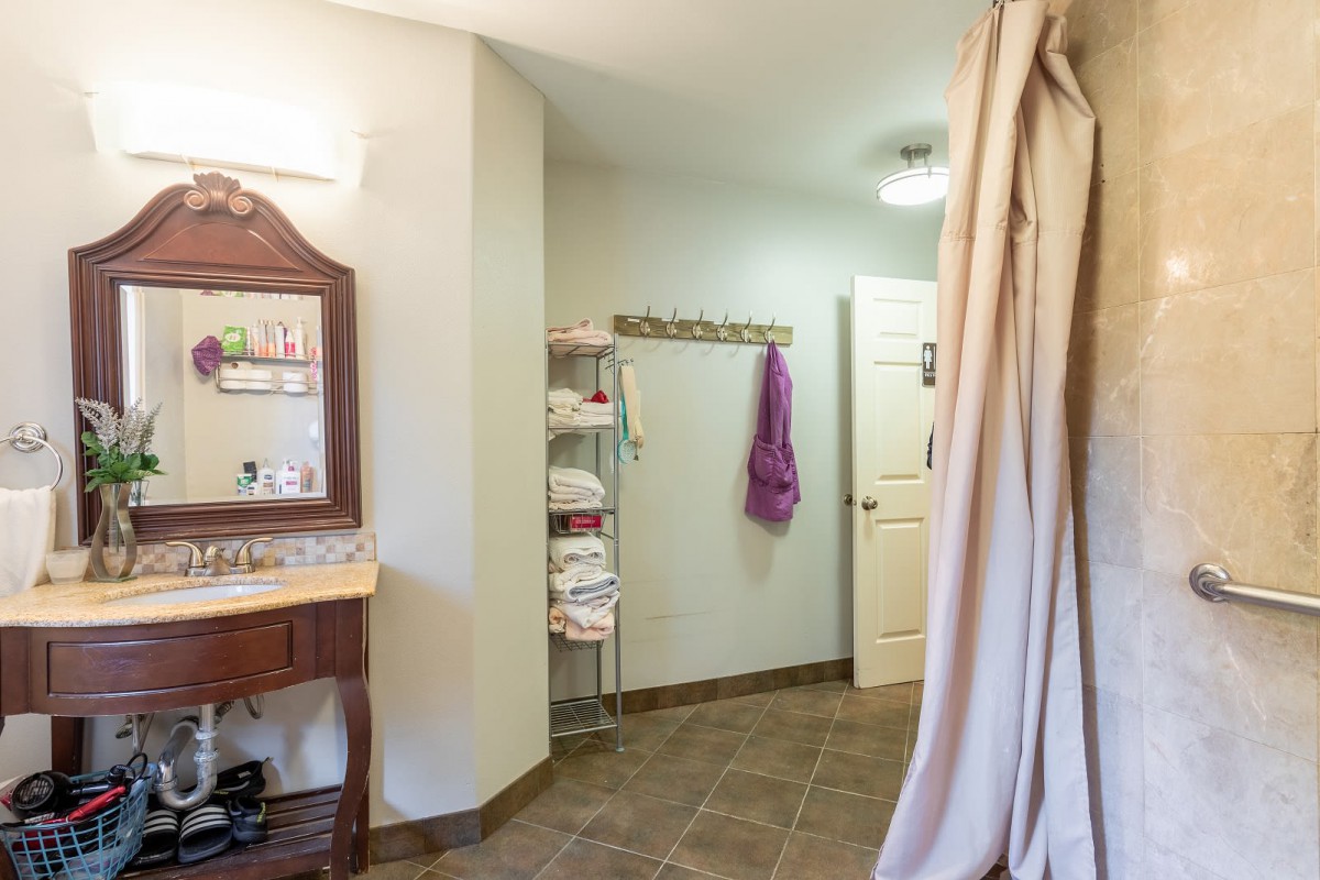 A spacious bathroom featuring a sink with a mirror, towel rack, and shower curtain.