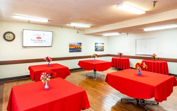 A well-decorated conference room featuring red tablecloths and floral centerpieces on each table, set up for an event or meeting.