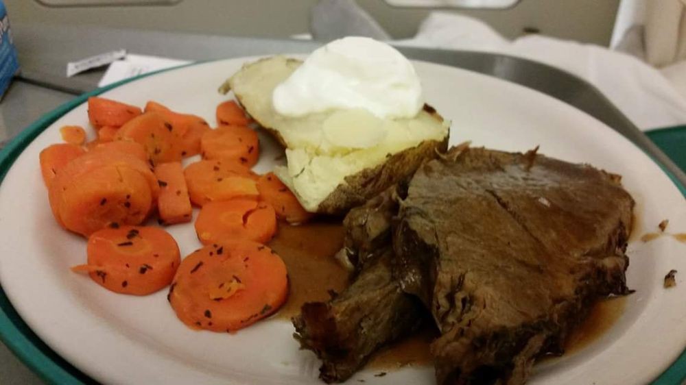 A plate featuring roast beef, sliced carrots, and a baked potato topped with sour cream.