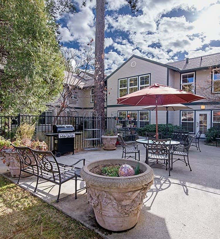A cozy patio area with outdoor furniture, a large umbrella, and lush greenery.