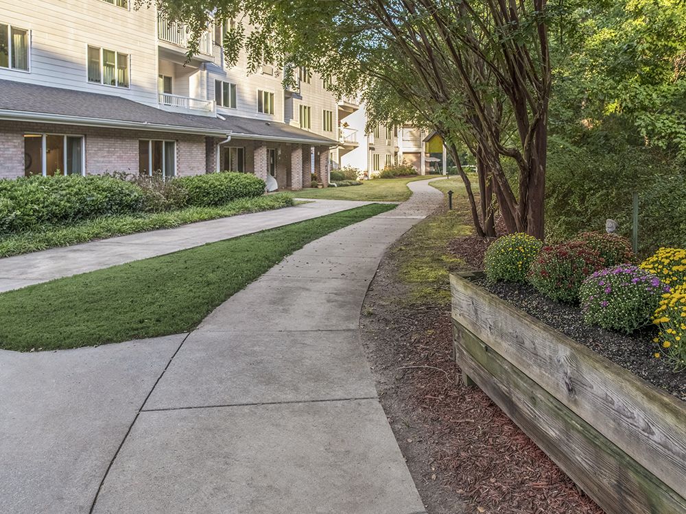 A curved sidewalk leads through landscaped greenery next to a residential building.