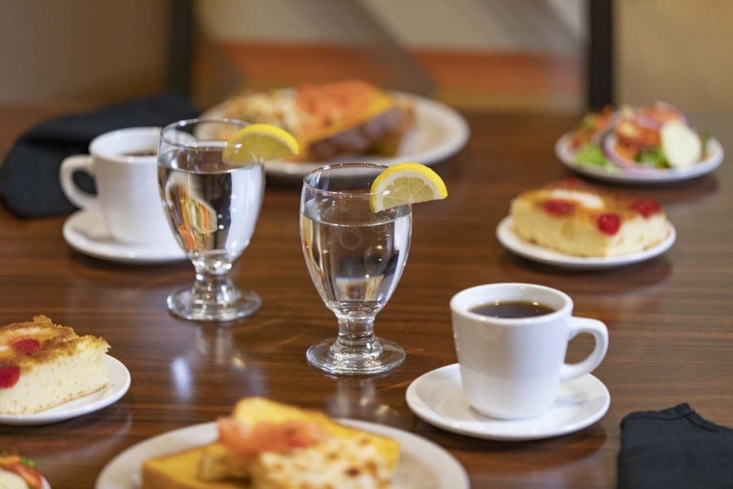 A breakfast table setting featuring coffee, water with lemon, and various dishes.