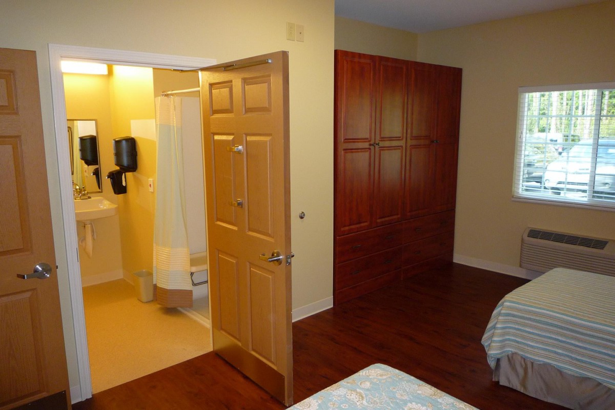 A cozy bedroom with a view of the bathroom entrance and wooden wardrobe.