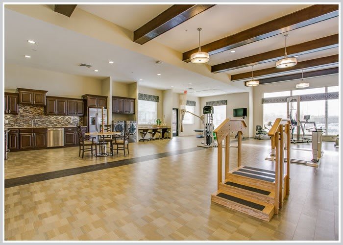 A spacious rehabilitation center featuring gym equipment, a kitchen area, and modern lighting.