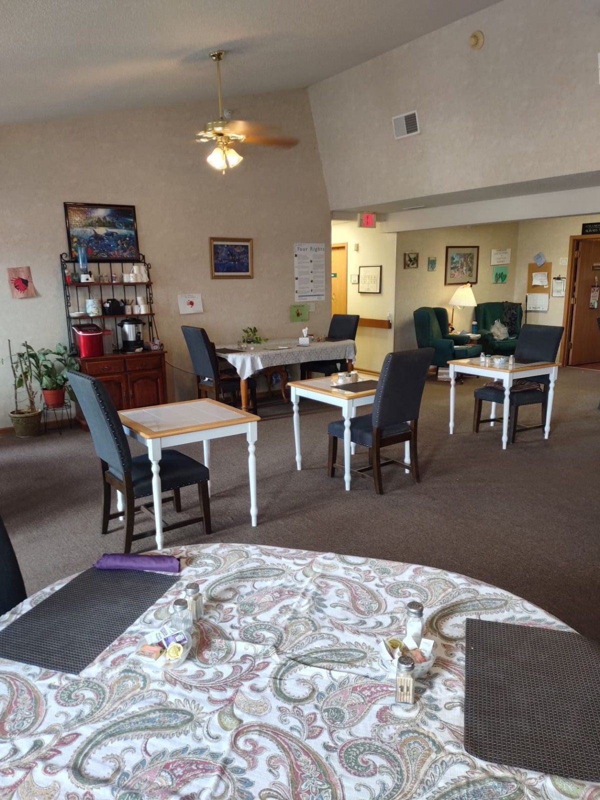 A cozy indoor dining area with neatly arranged tables and chairs, featuring a ceiling fan and warm decor.