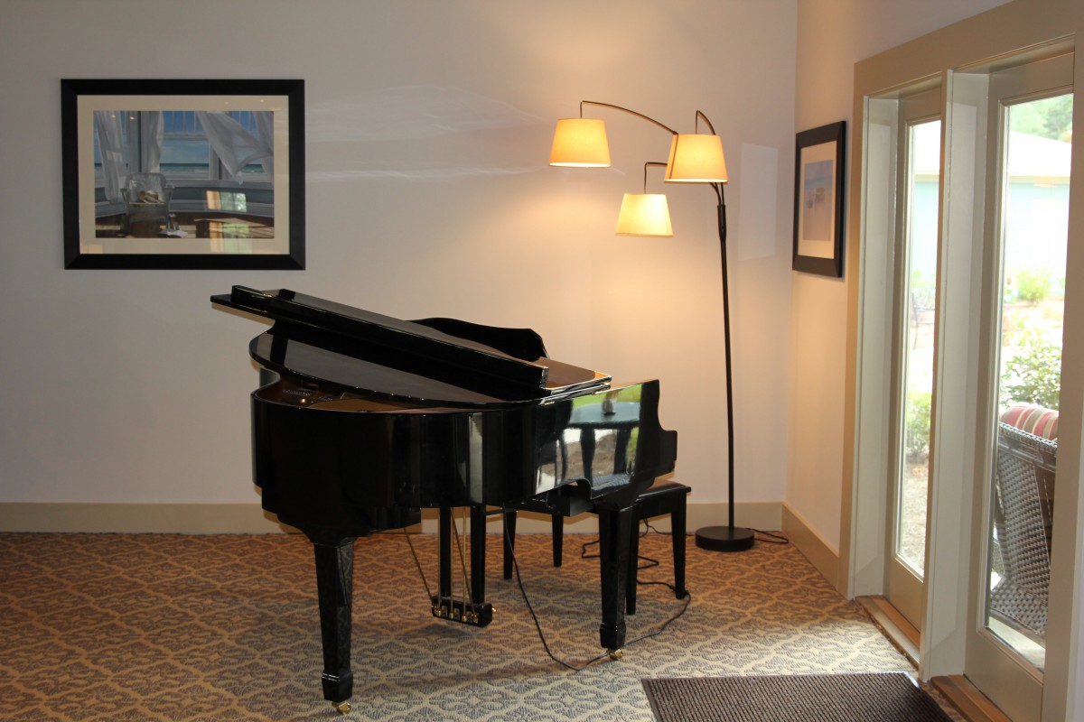 A cozy music room featuring a grand piano with a floor lamp and framed artwork.