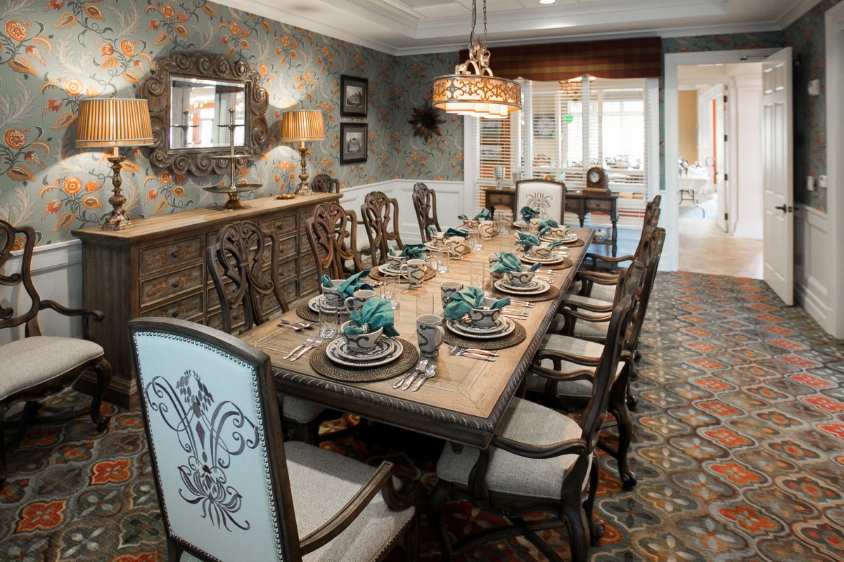 An elegantly designed dining room featuring a large table set for a formal meal with a chandelier overhead.