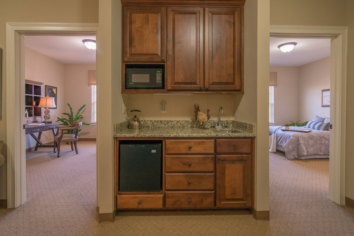 A compact kitchenette with wooden cabinets, a sink, and a microwave.