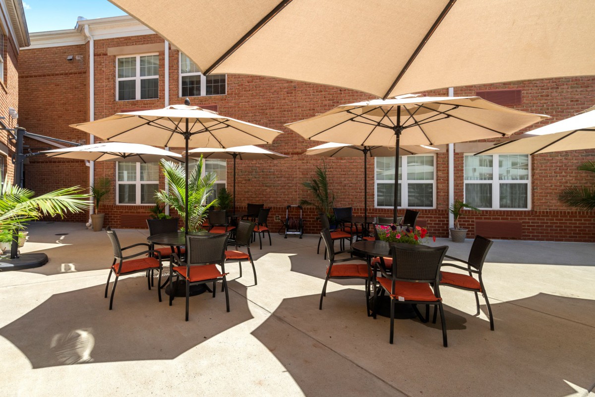 A sunny outdoor patio with tables and umbrellas in front of a brick building.