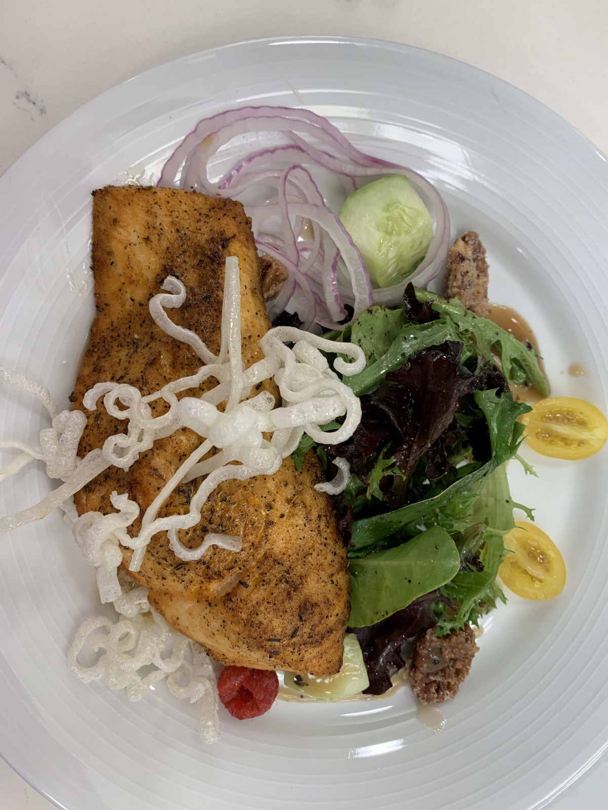 A plate featuring grilled fish served with fresh salad, including onions, cucumber, and various greens.
