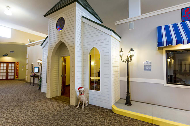 An indoor setting featuring a dog sitting beside a small building replica with Gothic-style windows and a lamp post.