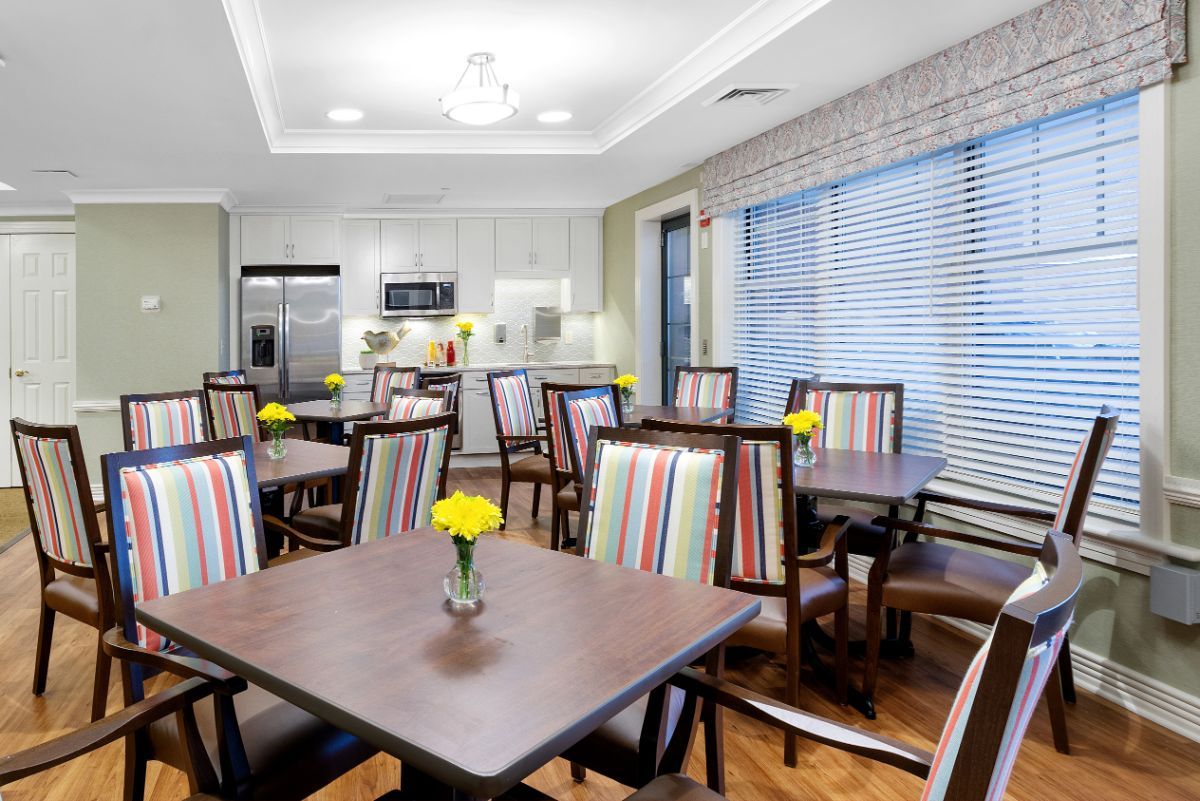 A modern dining area with neatly arranged tables and colorful striped chairs, featuring a kitchen in the background.