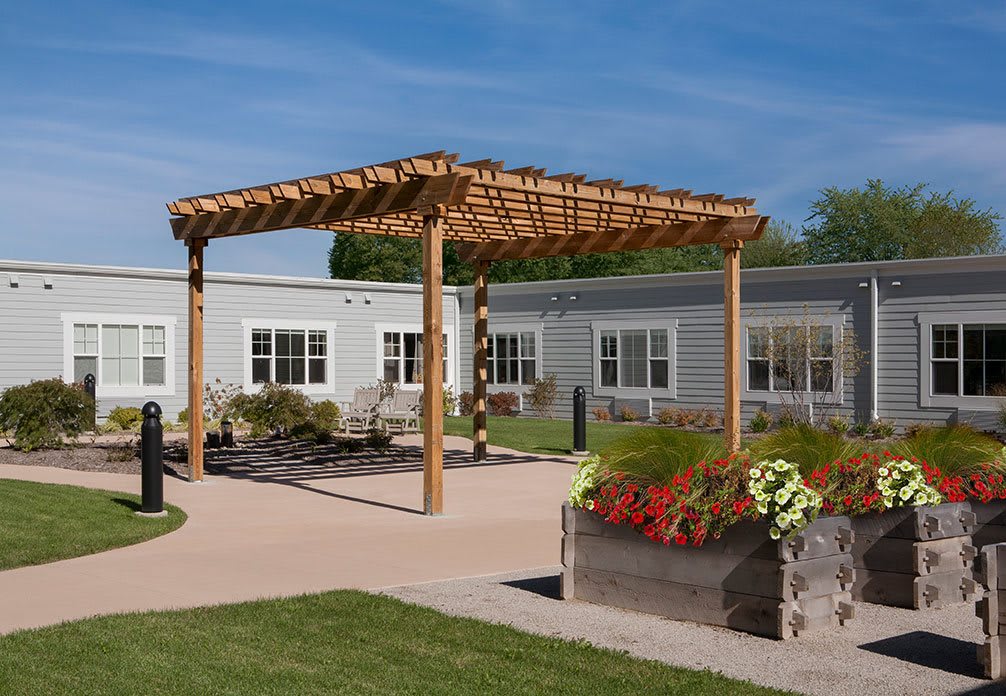 A serene outdoor area featuring a wooden pergola, flower beds, and modern architecture.