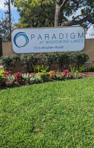 Entrance sign for Paradigm at Woodland Lakes, surrounded by vibrant landscaping.