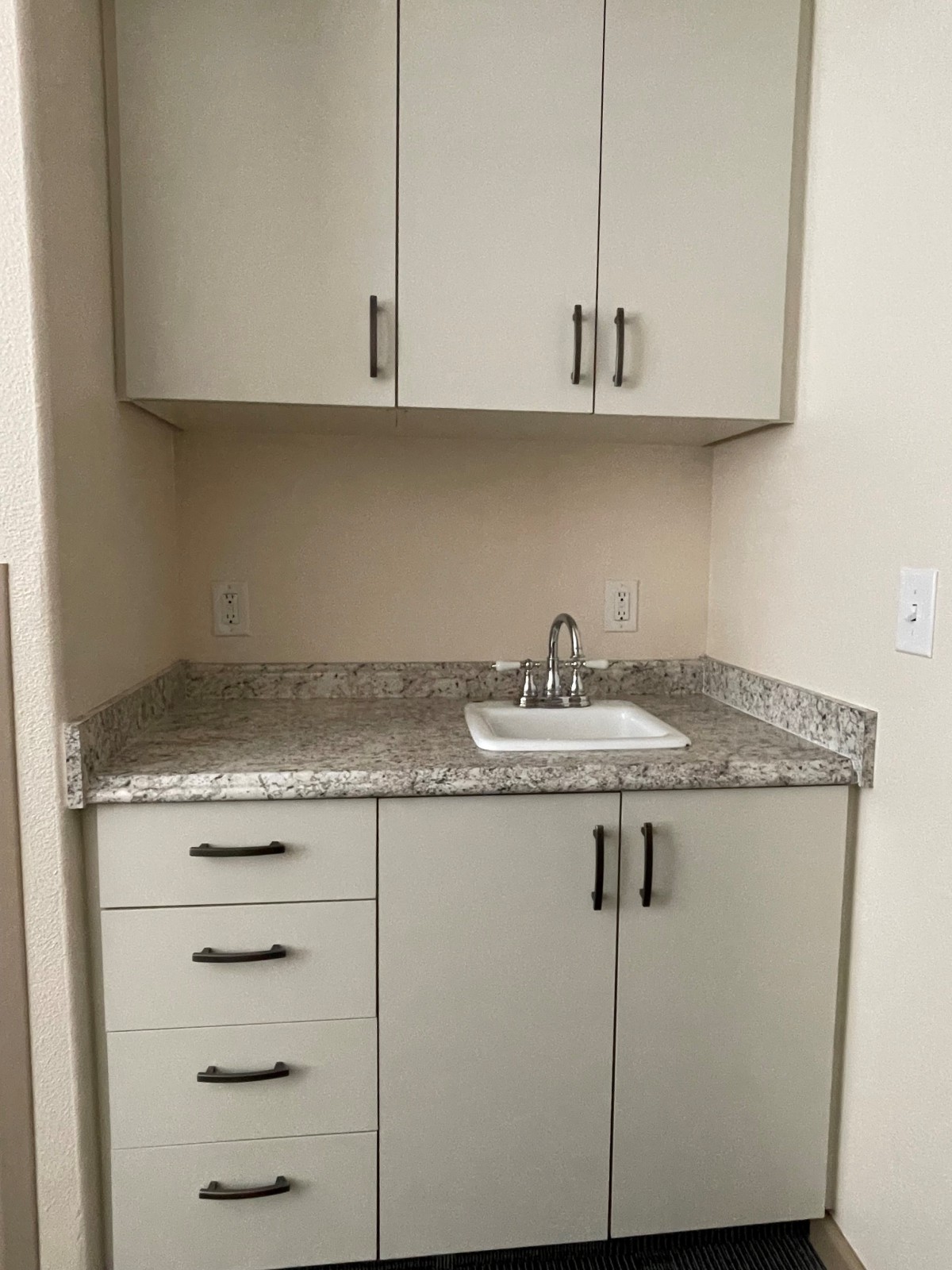 A small kitchen area with upper and lower cabinets, a countertop, and a sink.