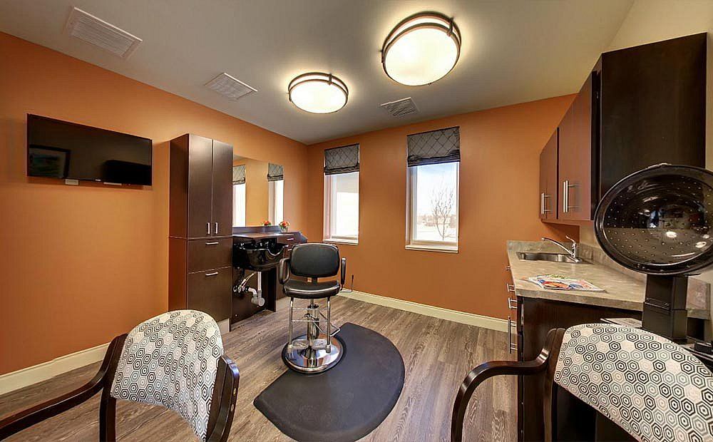 A cozy hair salon interior with a central barber chair, surrounded by mirrors and orange walls, featuring wooden flooring and modern lighting fixtures.