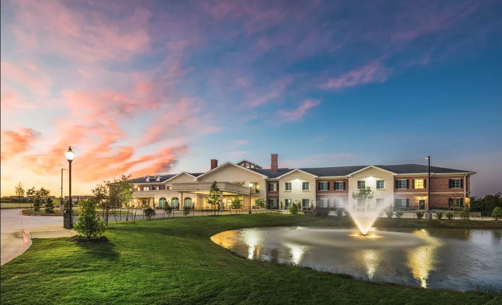 A picturesque view of a large building with a fountain and pond at sunset.
