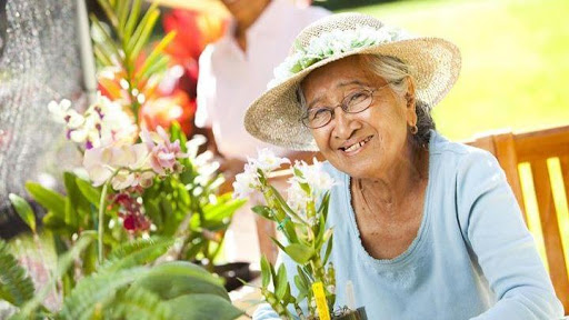 An elderly woman joyfully tending to her garden, surrounded by vibrant flowers.