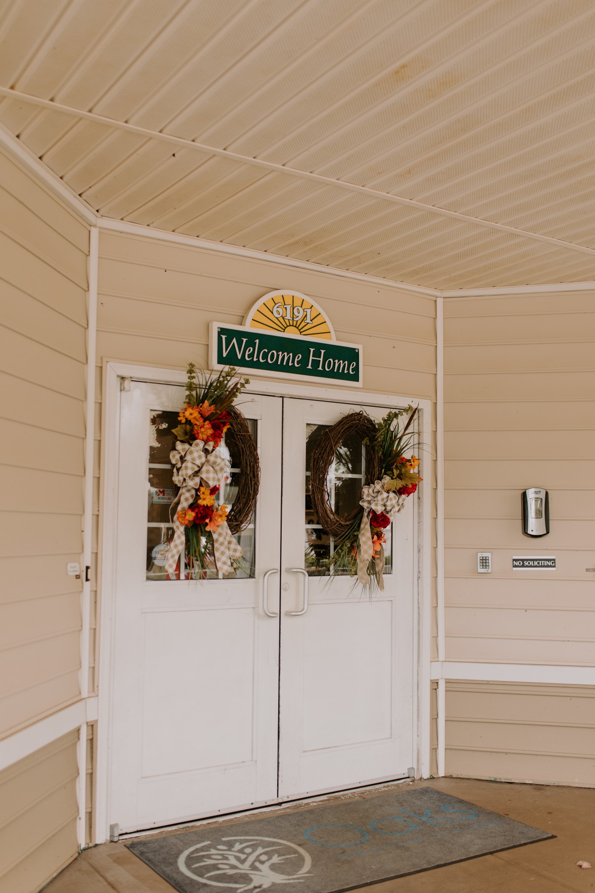 An entrance decorated with autumn-themed wreaths and a 'Welcome Home' sign.