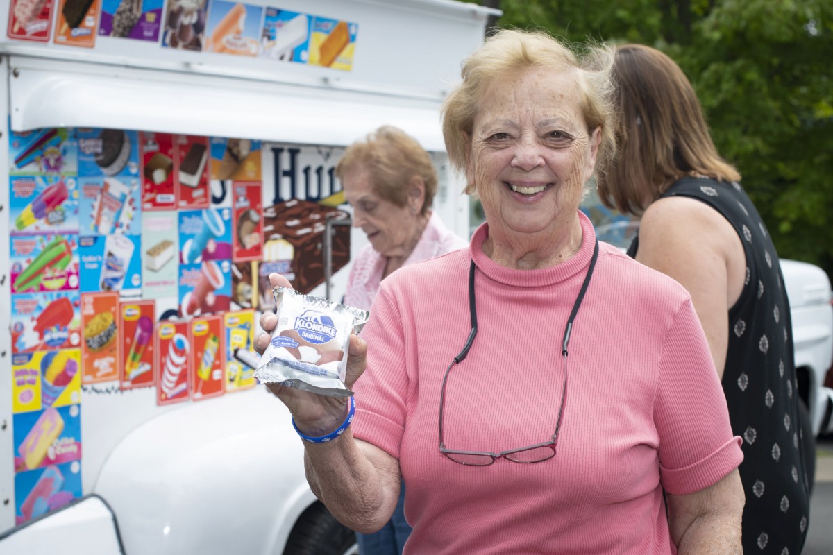 A woman in a pink shirt smiling while holding an ice cream cone in front of an ice cream truck.