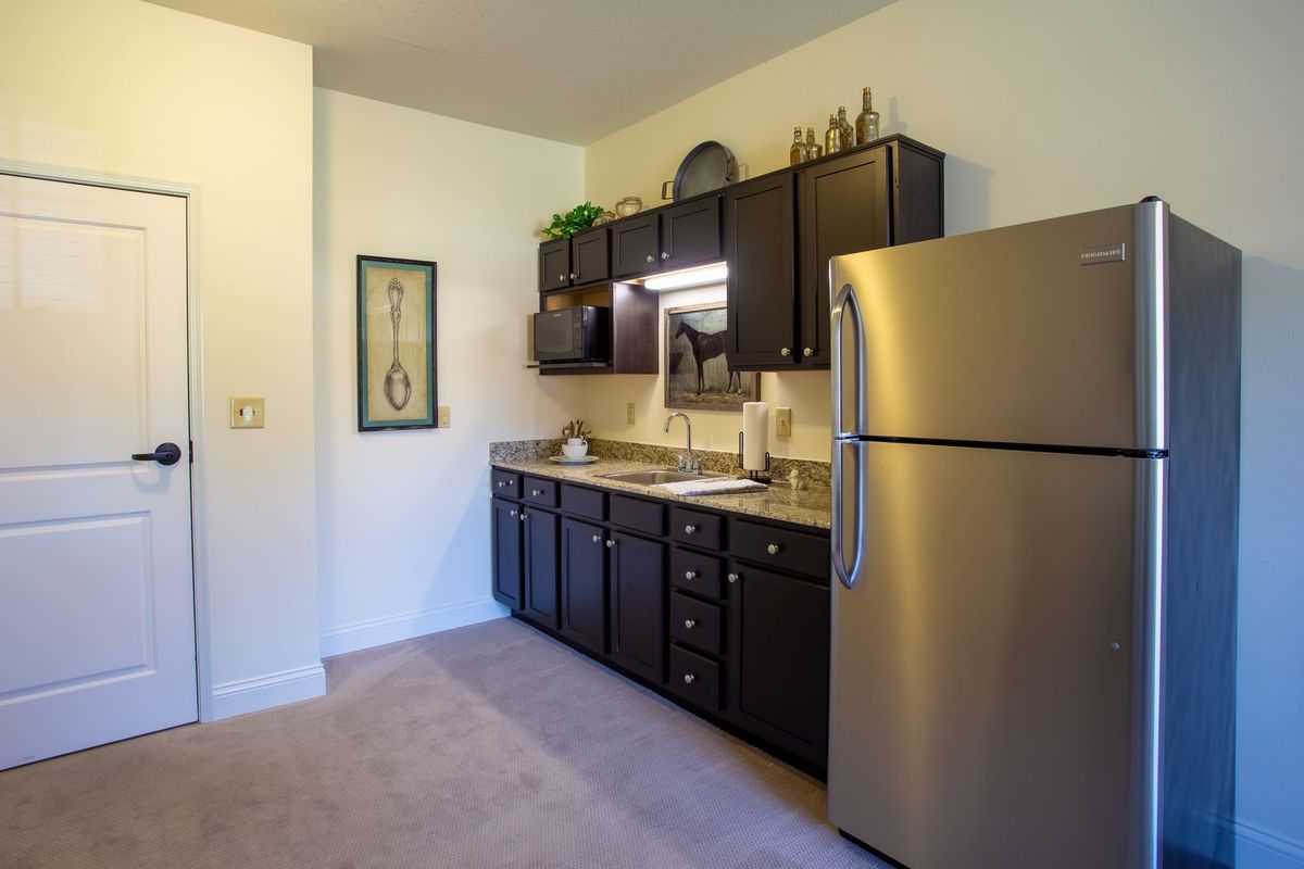 A modern apartment kitchen with dark cabinets and a stainless steel fridge.